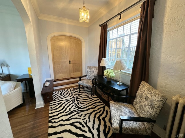 foyer with arched walkways, wood finished floors, ornamental molding, a textured wall, and a notable chandelier