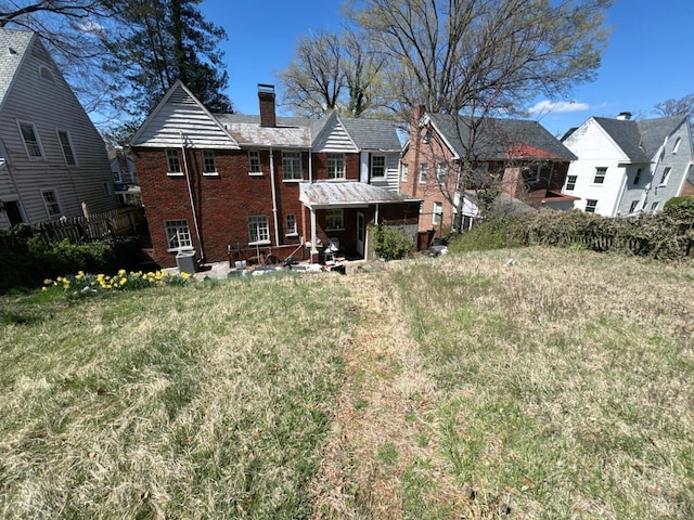 back of house with a residential view, a chimney, fence, a yard, and brick siding