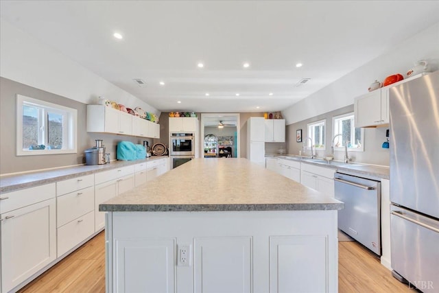 3554 Leffel Rd, Roanoke, VA 24018 - kitchen featuring appliances with stainless steel finishes, a center island, white cabinetry, a sink, and light wood-style flooring