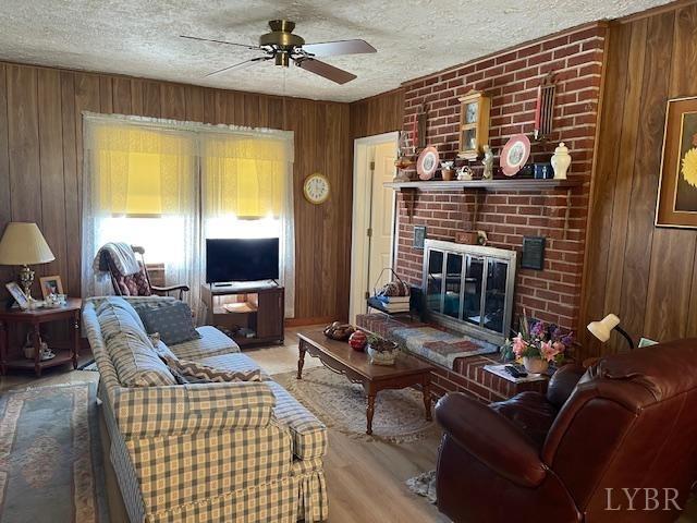 1534 Main St, Altavista, VA 24517 - living room featuring wooden walls, a brick fireplace, a textured ceiling, and ceiling fan