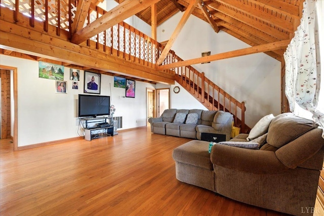 living area featuring stairs, high vaulted ceiling, wood finished floors, baseboards, and beamed ceiling