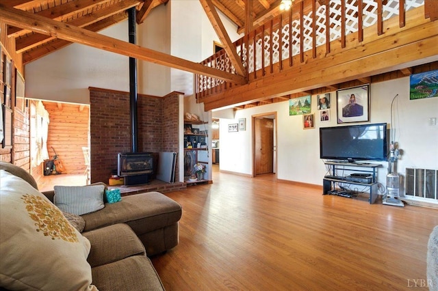 living area featuring visible vents, baseboards, wood finished floors, vaulted ceiling with beams, and a wood stove