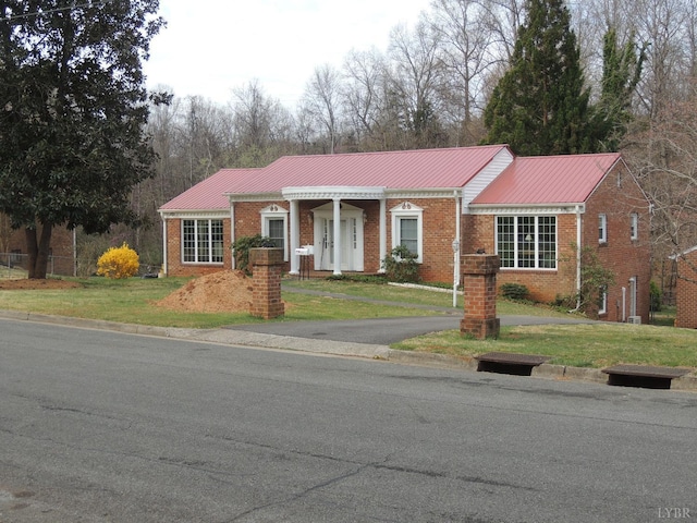 view of front of home with brick siding, a front yard, and metal roof