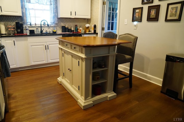 203 Marshall St, Brookneal, VA 24528 - kitchen with a sink, a breakfast bar area, dark countertops, decorative backsplash, and white cabinetry