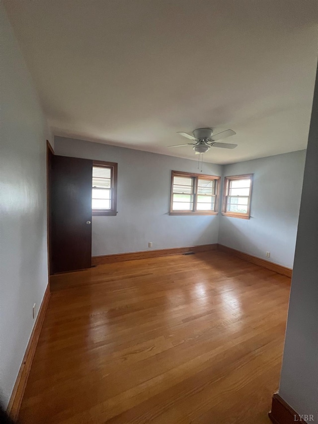 unfurnished room featuring baseboards, wood finished floors, and a wealth of natural light