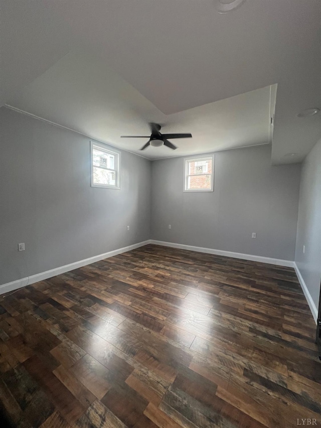 empty room with dark wood-style flooring, a ceiling fan, baseboards, and a wealth of natural light