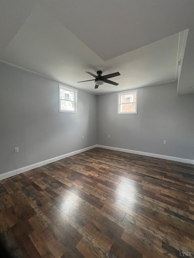 empty room featuring baseboards, plenty of natural light, a ceiling fan, and dark wood-style flooring