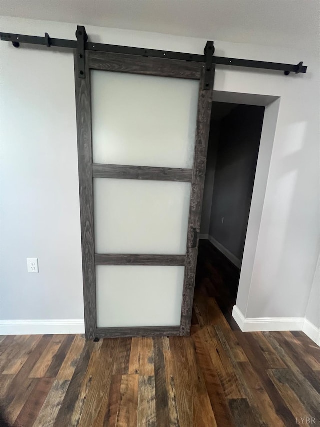 unfurnished room with baseboards, a barn door, and wood finished floors