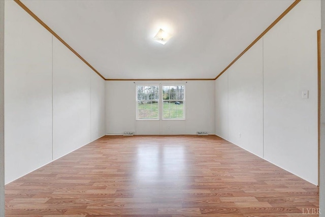 empty room with light wood-style flooring, visible vents, vaulted ceiling, and ornamental molding