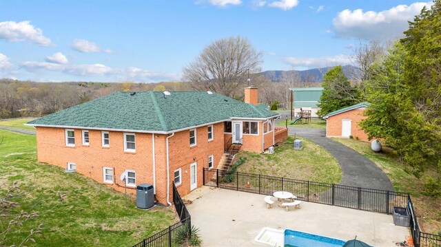 back of property featuring a chimney, brick siding, a patio, a shingled roof, and stairs