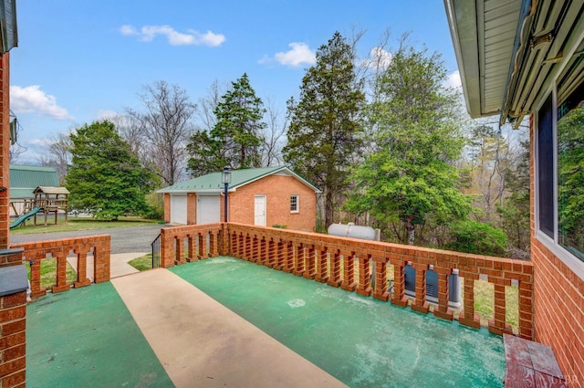 wooden terrace featuring a garage, an outbuilding, a playground, and a patio