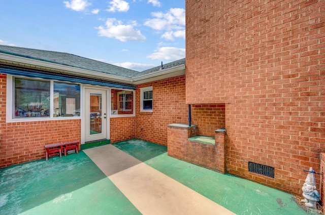 property entrance with brick siding, a patio, and roof with shingles
