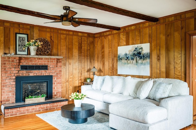 living area with beamed ceiling, ceiling fan, wood finished floors, a brick fireplace, and wooden walls