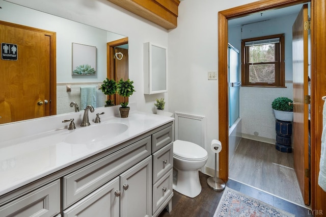 bathroom with wood finished floors, toilet, tile walls, vanity, and bathing tub / shower combination
