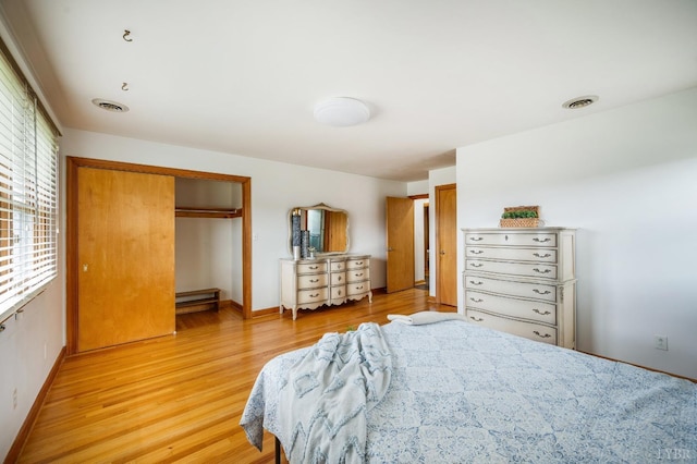 bedroom with light wood finished floors, a baseboard heating unit, baseboards, and a closet