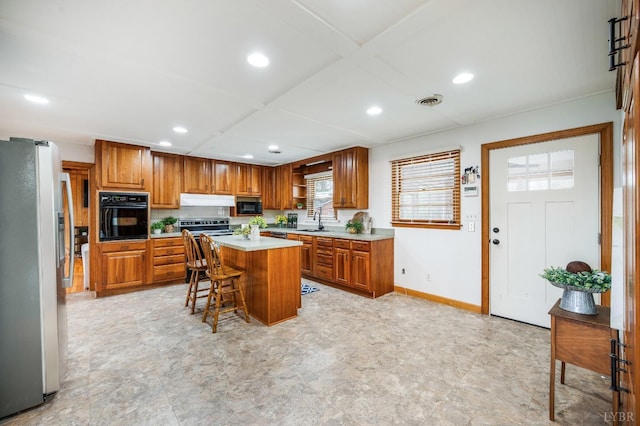 kitchen featuring black appliances, a sink, recessed lighting, brown cabinetry, and light countertops