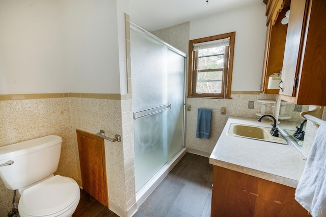 bathroom featuring toilet, a stall shower, vanity, wood finished floors, and tile walls