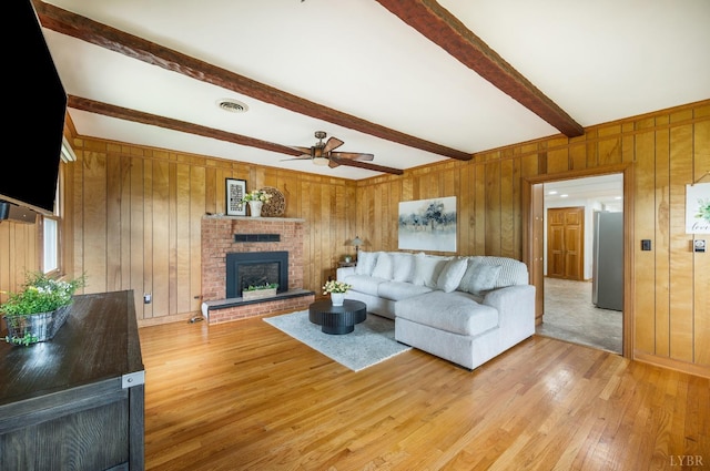 living area featuring beamed ceiling, a ceiling fan, light wood-style floors, a fireplace, and wood walls