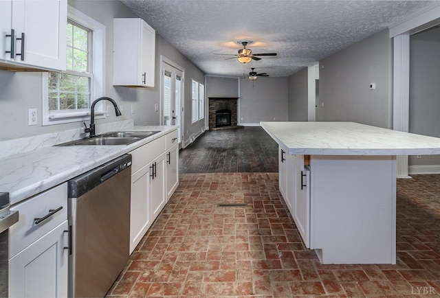 108 Trapper Ln, Vinton, VA 24179 - kitchen with stainless steel dishwasher, a sink, a ceiling fan, a fireplace with raised hearth, and white cabinetry