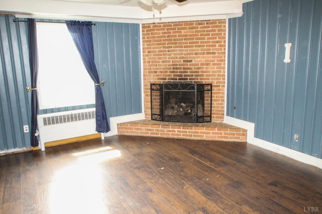 1428 Club Dr, Lynchburg, VA 24503 - unfurnished living room featuring radiator heating unit, a ceiling fan, hardwood / wood-style floors, a brick fireplace, and wood walls
