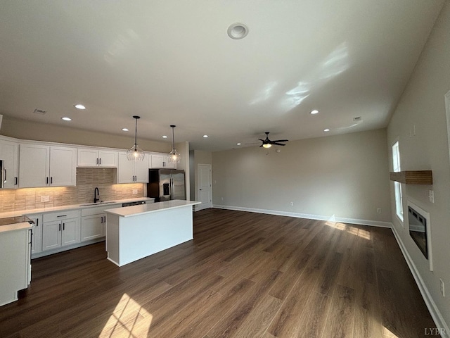 kitchen featuring a ceiling fan, a center island, stainless steel fridge, tasteful backsplash, and a glass covered fireplace
