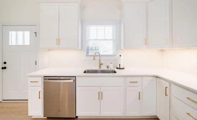 kitchen with stainless steel dishwasher, tasteful backsplash, a sink, light countertops, and white cabinets