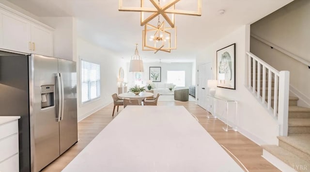 interior space featuring white cabinets, stainless steel fridge, light wood-style floors, and a notable chandelier