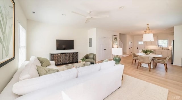 living room featuring electric panel, light wood-style flooring, visible vents, and a ceiling fan