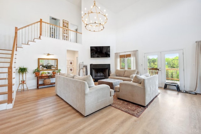 living area with an inviting chandelier, wood finished floors, a high ceiling, a fireplace, and stairs