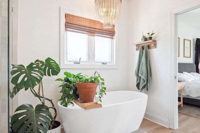 ensuite bathroom featuring a notable chandelier, baseboards, ensuite bath, a soaking tub, and wood finished floors