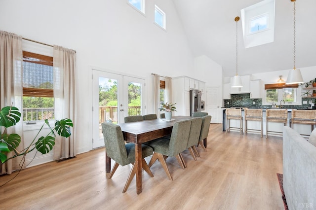 dining space featuring a skylight, french doors, light wood-type flooring, and a high ceiling