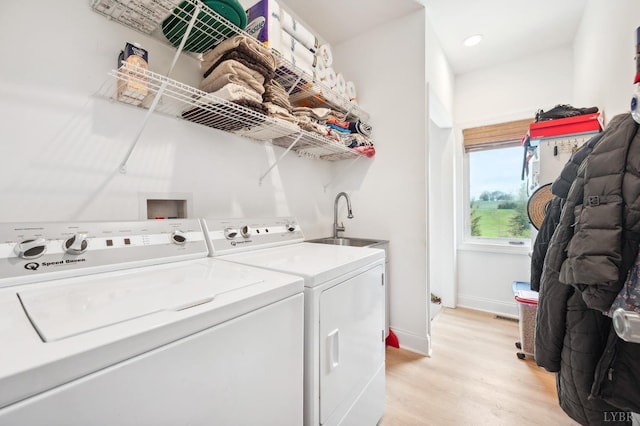 clothes washing area with light wood-style flooring, washing machine and dryer, baseboards, a sink, and laundry area