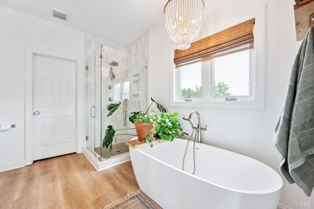 bathroom featuring wood finished floors, a stall shower, a notable chandelier, visible vents, and a freestanding tub