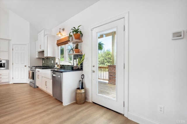 kitchen with light wood-style flooring, dark countertops, stainless steel appliances, white cabinets, and tasteful backsplash