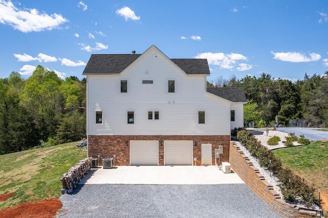 view of home's exterior featuring an attached garage, brick siding, a yard, cooling unit, and gravel driveway