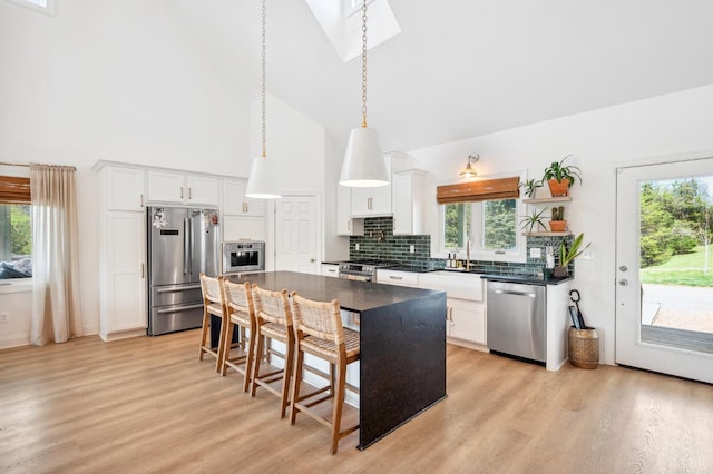 kitchen with high vaulted ceiling, dark countertops, appliances with stainless steel finishes, and light wood-style floors
