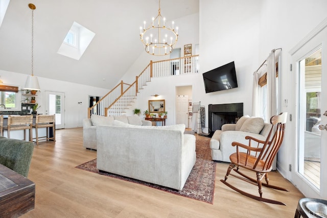 living area featuring high vaulted ceiling, stairway, a fireplace, light wood-type flooring, and a skylight