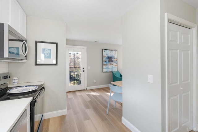 442 W King St, Bedford, VA 24523 - kitchen featuring light wood finished floors, stainless steel microwave, baseboards, white cabinetry, and black range with electric stovetop