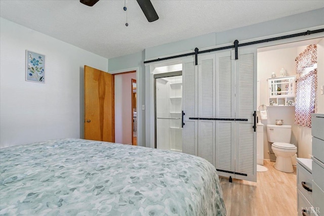 1321 Norfolk Ave, Bedford, VA 24523 - bedroom featuring a barn door, light wood-style floors, a textured ceiling, ceiling fan, and connected bathroom