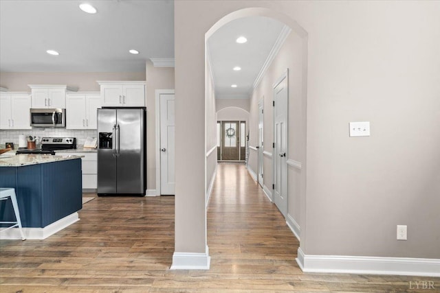 kitchen with white cabinets, arched walkways, stainless steel appliances, wood finished floors, and ornamental molding