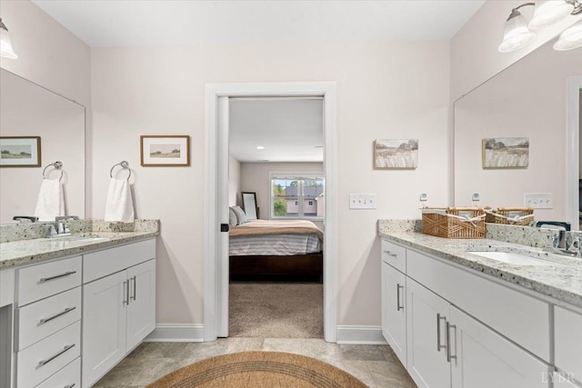 ensuite bathroom featuring baseboards, two vanities, a sink, and ensuite bath