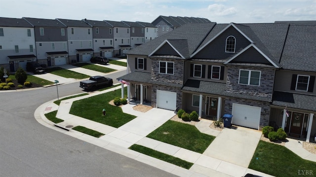 townhome / multi-family property featuring a residential view, stone siding, a garage, a front yard, and driveway