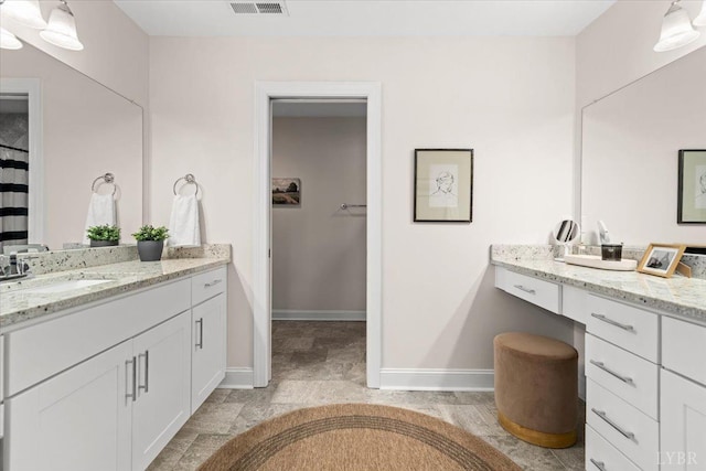bathroom featuring a sink, baseboards, a spacious closet, and two vanities
