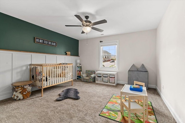 bedroom with a nursery area, baseboards, a ceiling fan, and carpet flooring