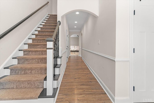 stairs with ornamental molding, wood finished floors, baseboards, recessed lighting, and arched walkways