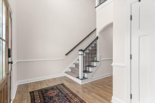 foyer entrance with baseboards, arched walkways, stairs, and wood finished floors