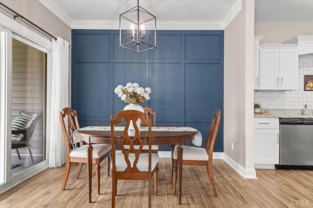 dining area with baseboards, light wood finished floors, a chandelier, ornamental molding, and a decorative wall