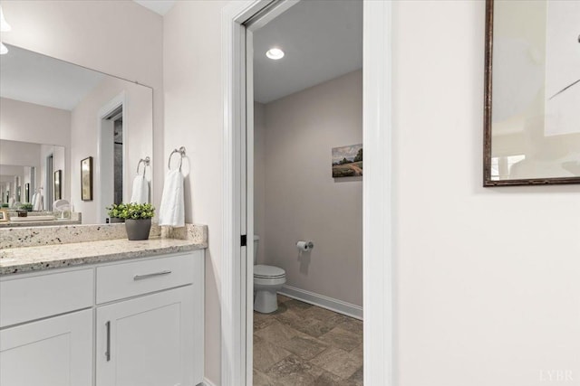 bathroom featuring vanity, toilet, recessed lighting, baseboards, and stone finish flooring