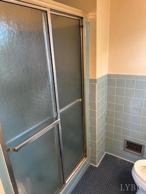 116 Carson St, Brookneal, VA 24528 - bathroom with a stall shower, toilet, tile patterned flooring, tile walls, and a wainscoted wall