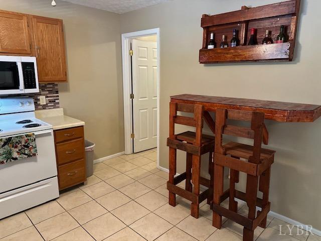 301 Gooseneck Ct, Forest, VA 24551 - kitchen with white range with electric cooktop, tasteful backsplash, light tile patterned flooring, baseboards, and brown cabinets